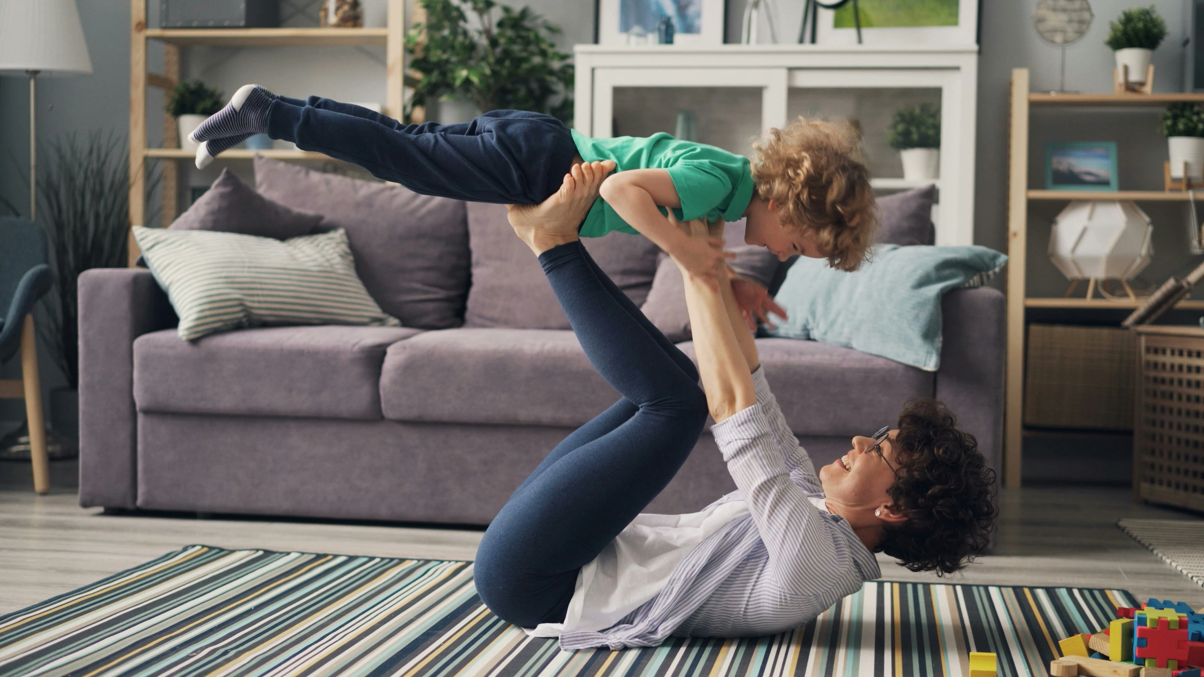 A smiling parent enjoying quality time with their child in a living room by lifting them up in the air with their hands and feet