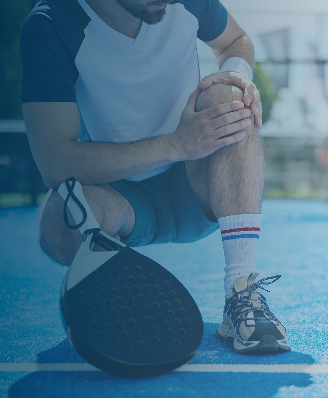 A person on a pickleball court kneeling down and holding his knee with his hands